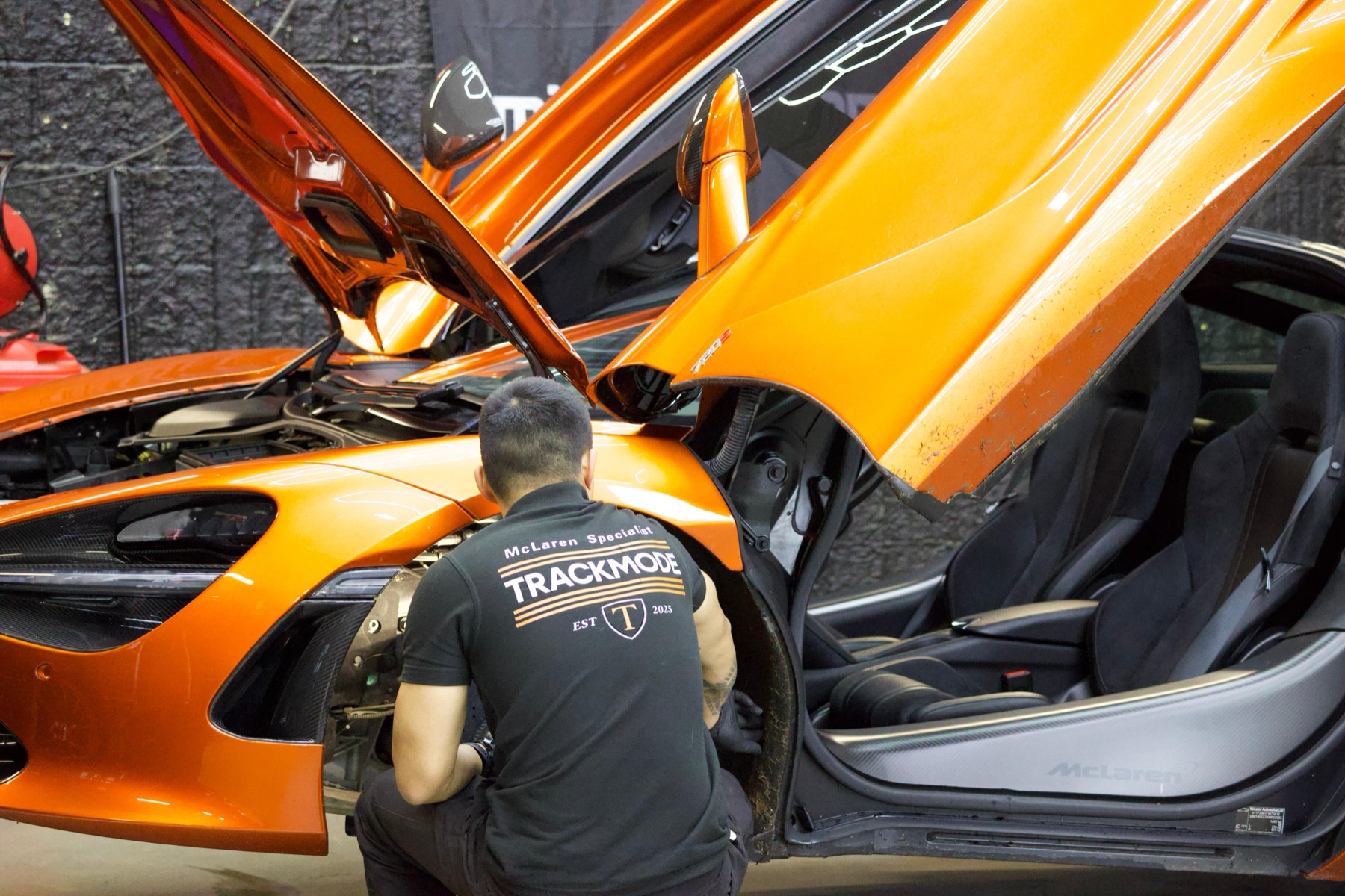 Technician beside an orange McLaren 720S with its doors open