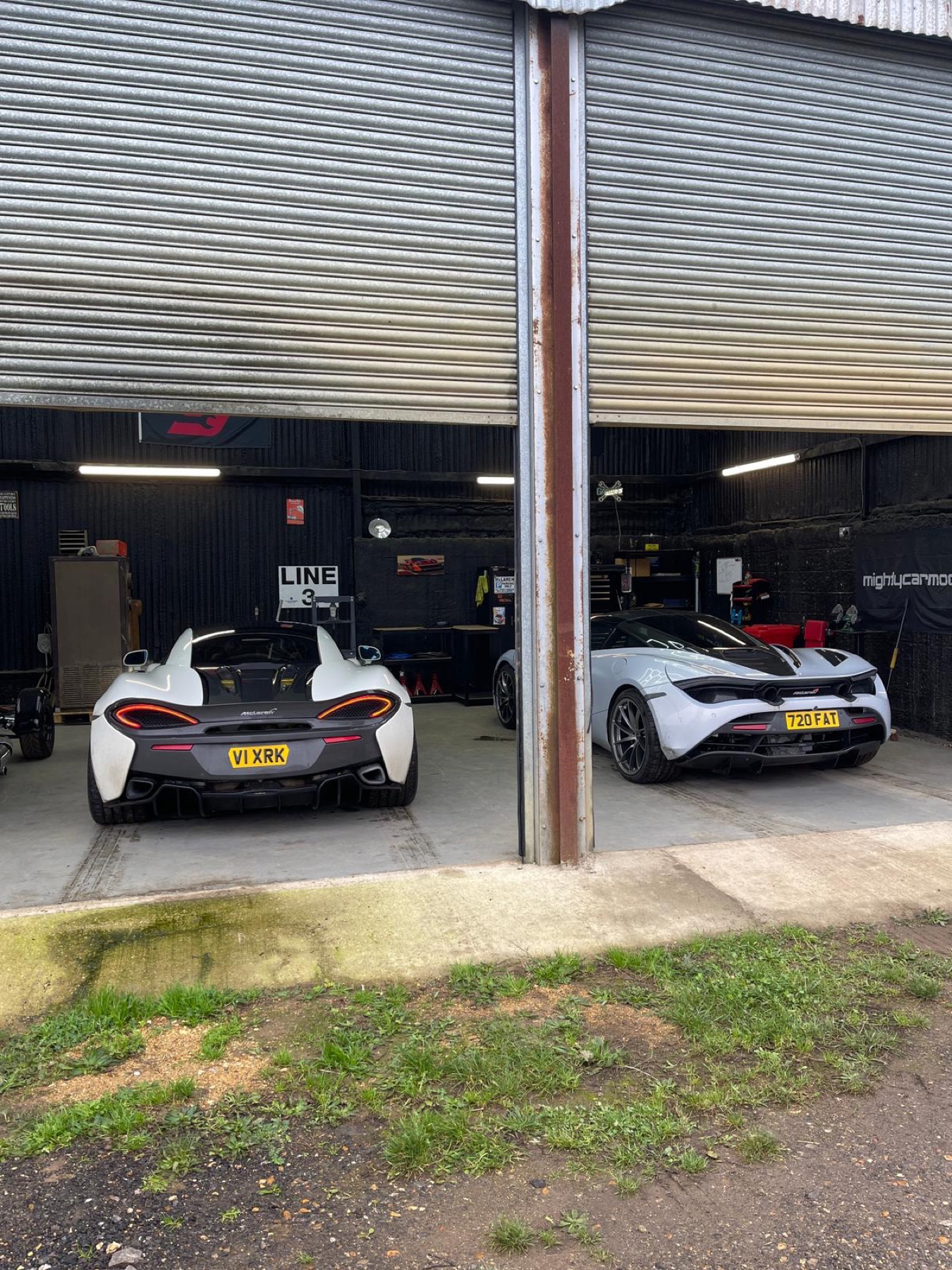 Two white McLarens parked in adjacent workshop bays